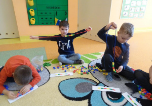 Dzieci nawlekają kształtki Numicon według wzoru na kartce na sznurek.